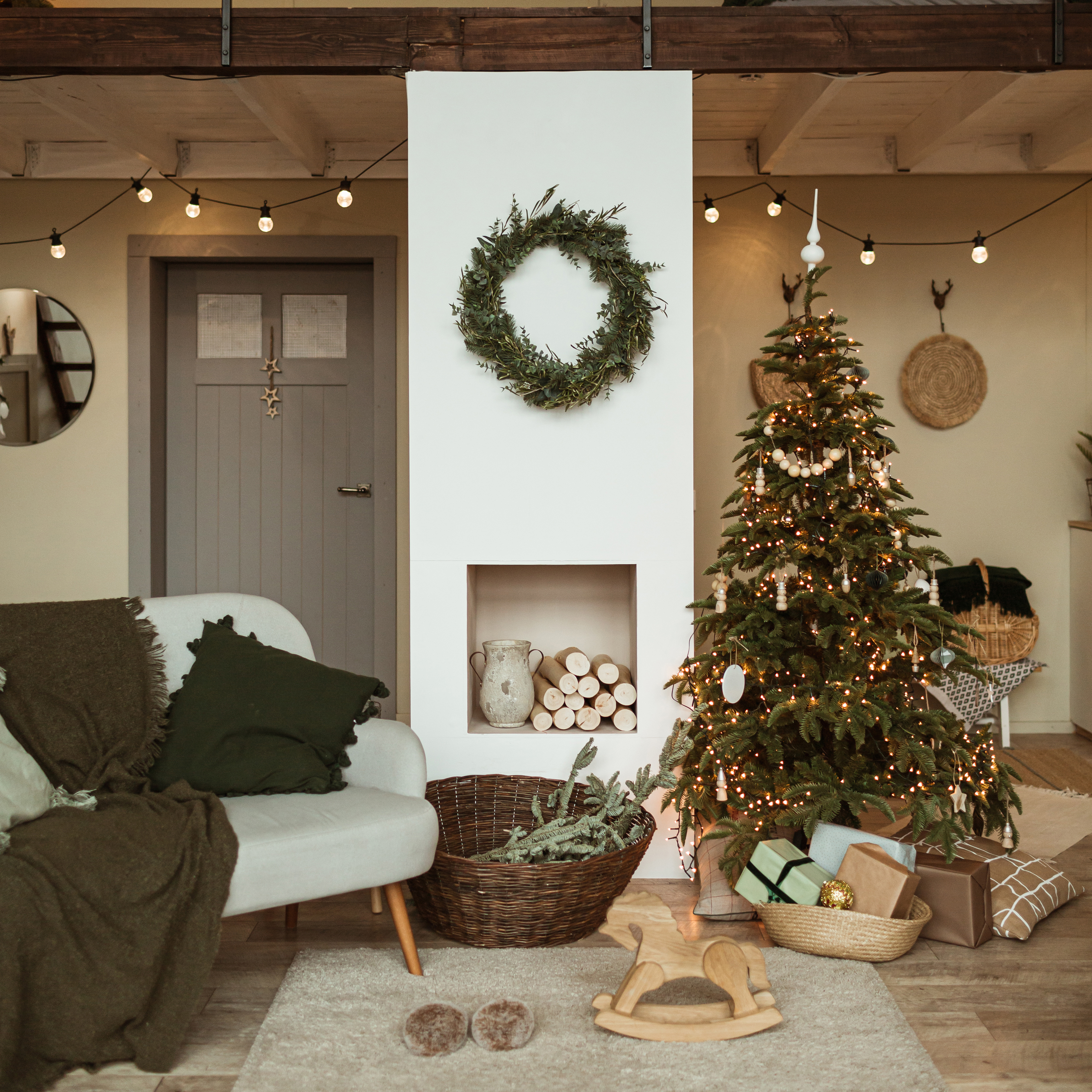 Modern interior design concept. Comfortable cozy living room decorated with Christmas tree with gifts, wreath frame, fireplace, sofa, carpet. Christmas / New Year celebration decorations